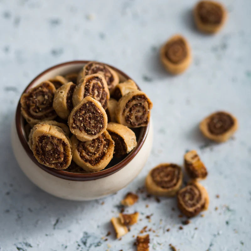 Almond House Bakharvadi served in a ceramic bowl with spiral snacks scattered on a light background