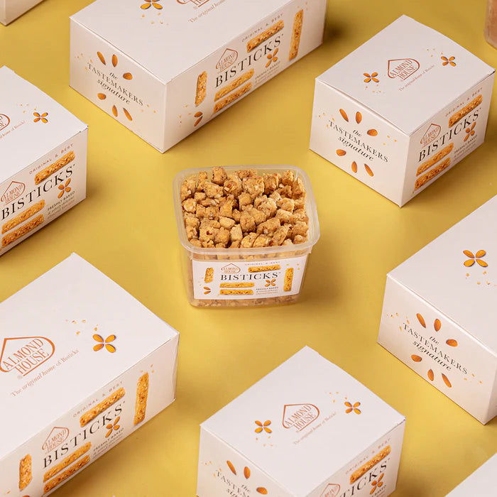 Almond House Bisticks container surrounded by multiple Almond House Bisticks gift boxes on a yellow background, showcasing premium packaging.