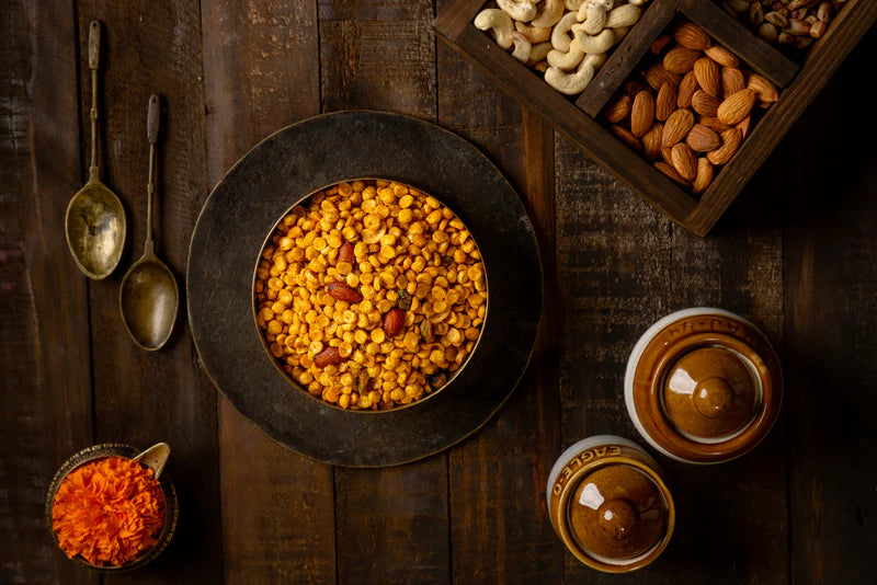 Top view of Chabina, a chickpea snack with almonds, surrounded by nuts, marigold petals, and vintage spoons.