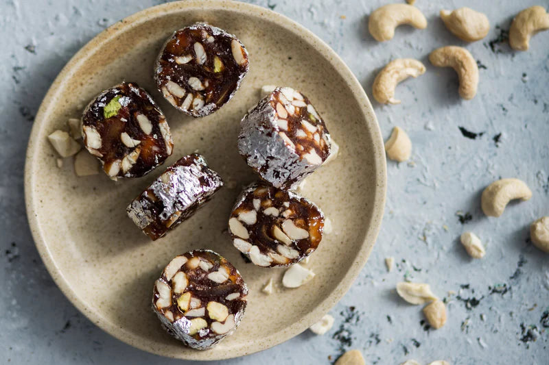 Almond House Kajoor Doller sweets made with dates and dry fruits, garnished with silver foil, served on a ceramic plate.