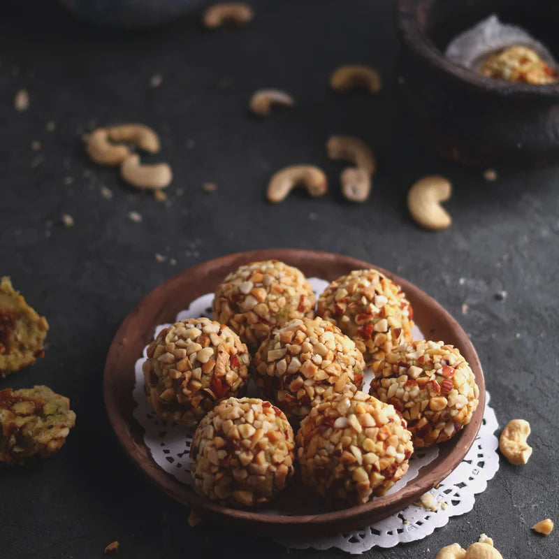 Almond House Kaju Dryfruit Laddu – gourmet Indian sweets made with crushed cashews, almonds, pistachios, gulkand and honey, served on a wooden plate.