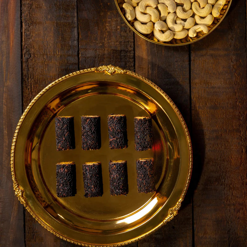 Almond House Kaju Flakes Roll served on a golden tray – rich Indian cashew sweets coated in chocolate sprinkles, elegantly arranged on a wooden background.