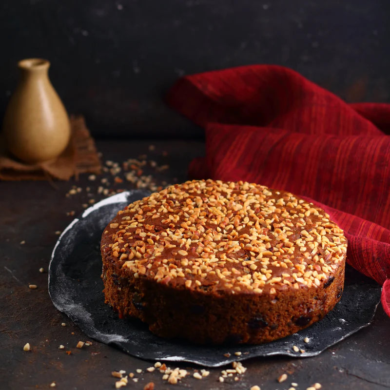 Side view of Almond House Plum Cake with nut topping, placed on a black plate and red cloth background.