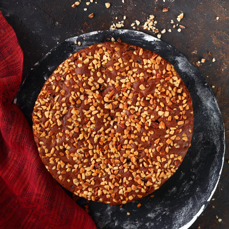 Top view of Almond House Plum Cake garnished with chopped nuts on a rustic black platter.