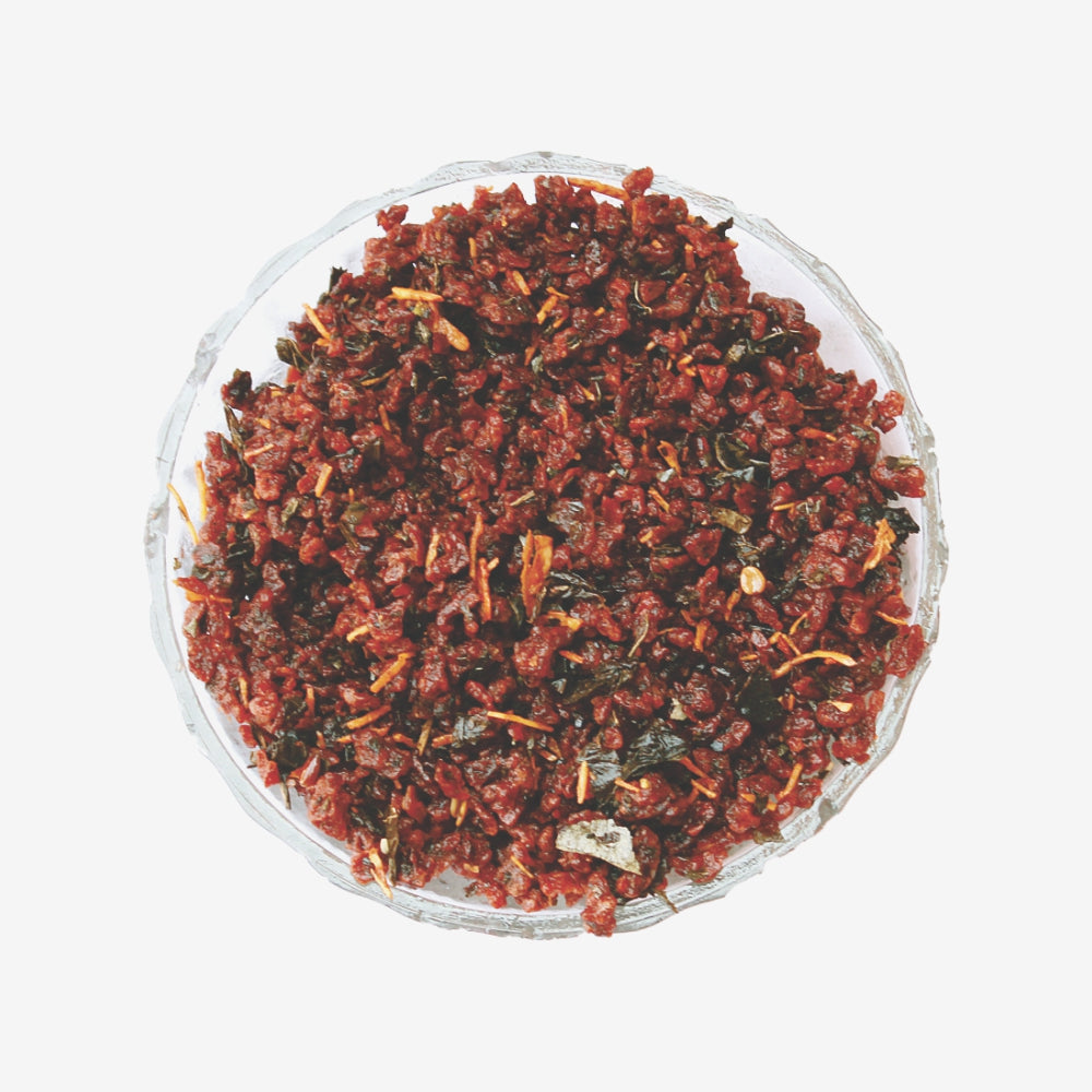 Dried red and green tea leaves in a glass bowl on a white background