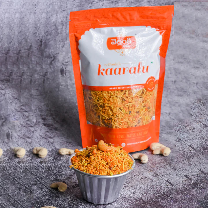 A bowl of Vellanki Foods Sanna Boondi Mixture with cashews, placed in front of a vibrant packaging, set against a textured gray background.