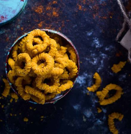 Almond House Chagodi, a traditional crispy and savory Indian snack, served in a rustic tin container with scattered pieces around.