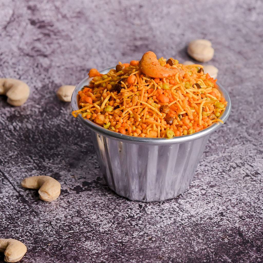 A bowl of Vellanki Foods Sanna Boondi Mixture with cashews, set against a textured gray background.