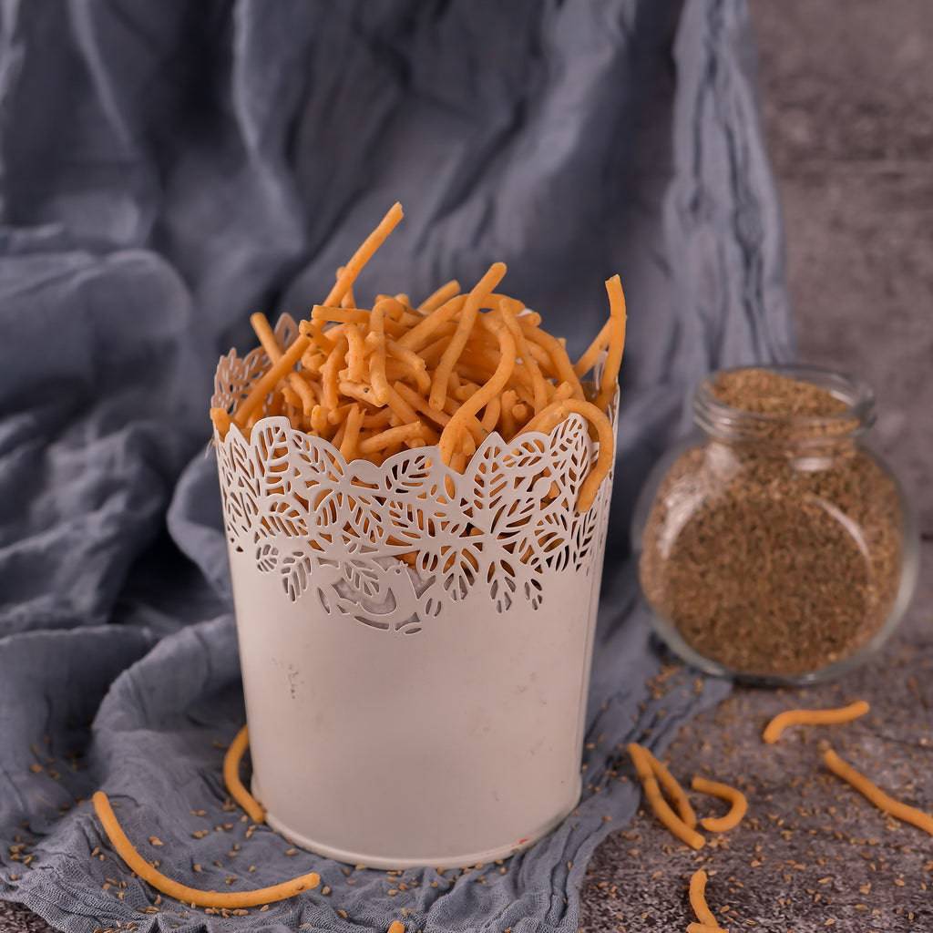 Vellanki Foods Vampoosa (Kaaralu) in a decorative white container with ajwain seeds displayed in the background on a fabric surface.