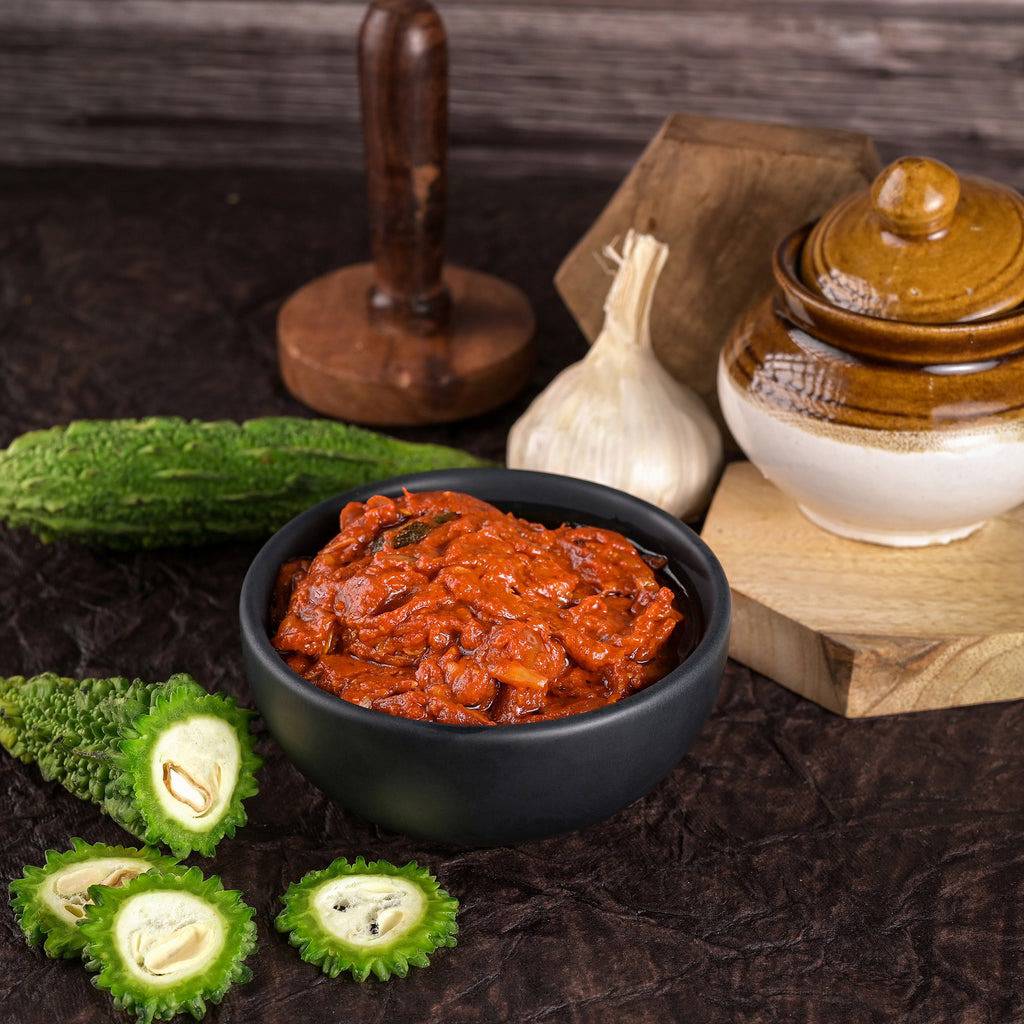 Vellanki Foods Bittergourd Pickle in a black bowl with fresh bittergourd slices and with rustic wooden surface.